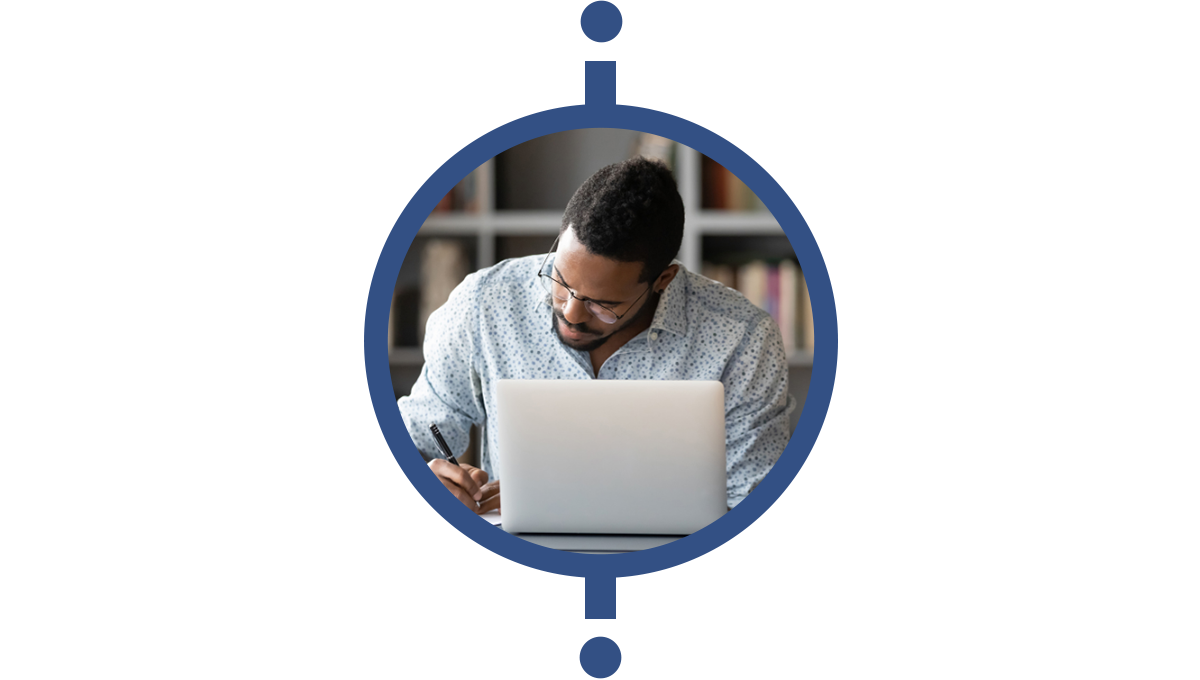 a man sits at a table looking at a computer and taking notes