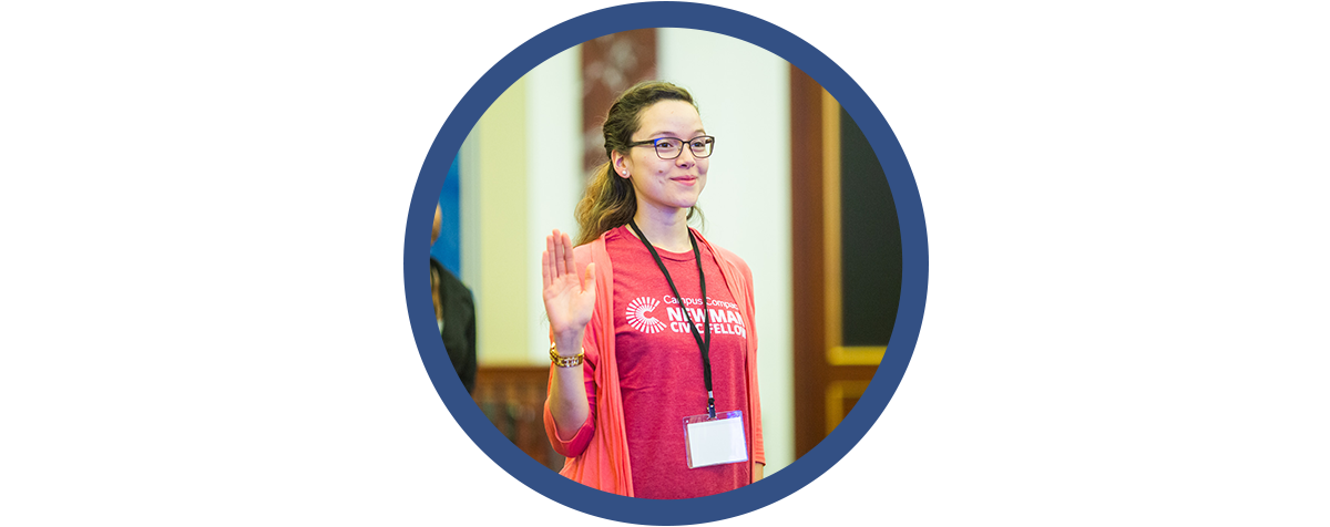 woman in newman civic fellows t-shirt raises her hand