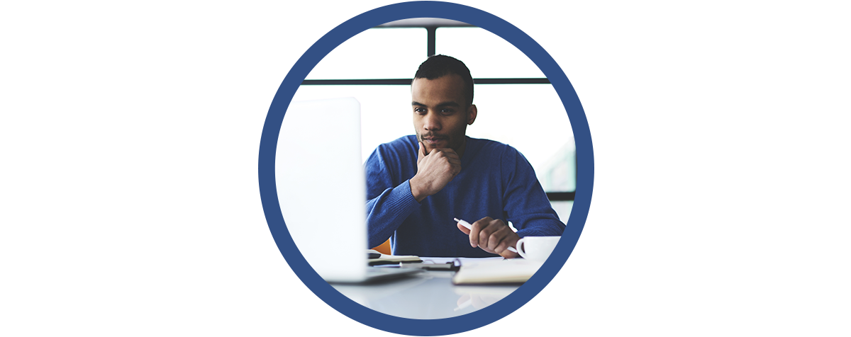 a man sits at a table looking at a computer and taking notes