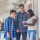 adult stands with two students, one taking notes