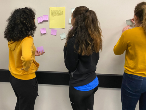 students putting post it notes on a white board