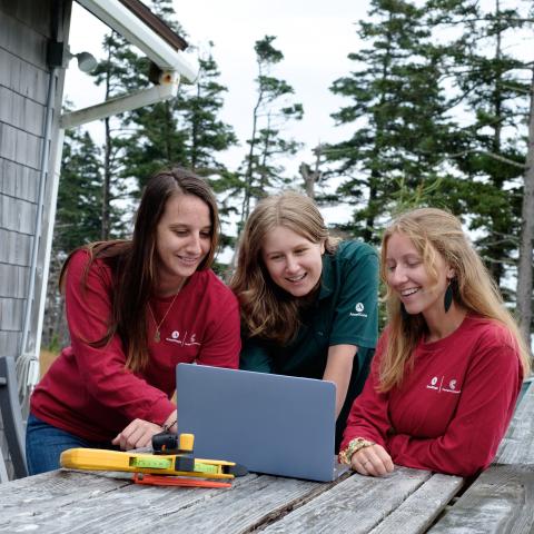 Three CCAC AmeriCorps members gathered around a laptop as they perform a home energy efficiency assessment. 